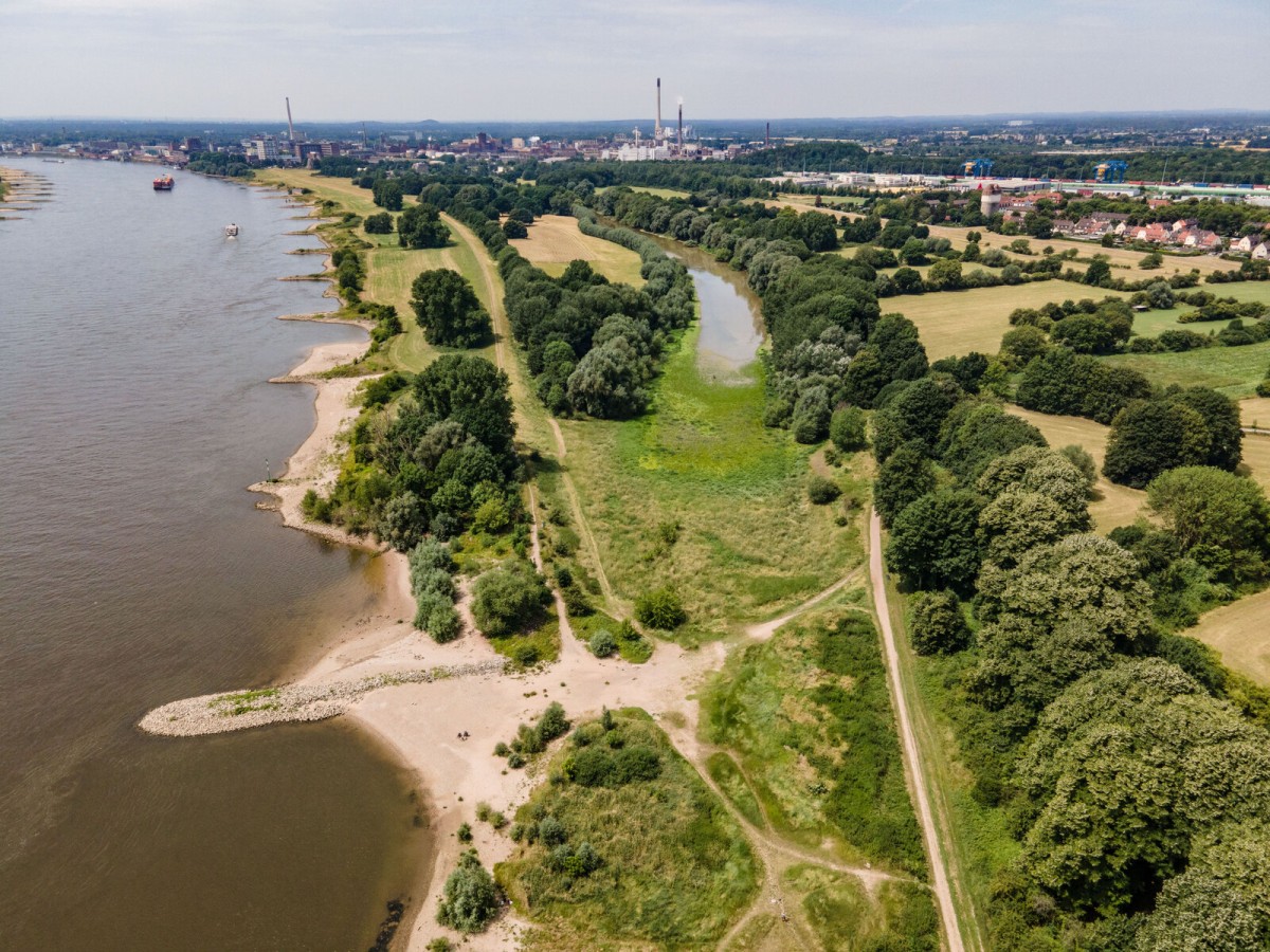 Luftaufnahme der Rheinaue bei Duisburg mit Auenlandschaft am Flussufer und Industrie am Horizont
